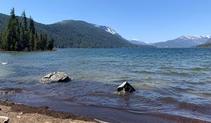 A windy lake with evergreens and snow capped peaks in the distance.